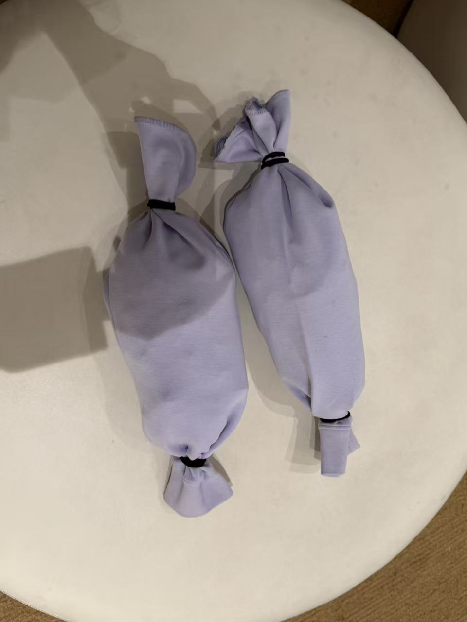 Two pale purple, elongated fabric toys tied at both ends.