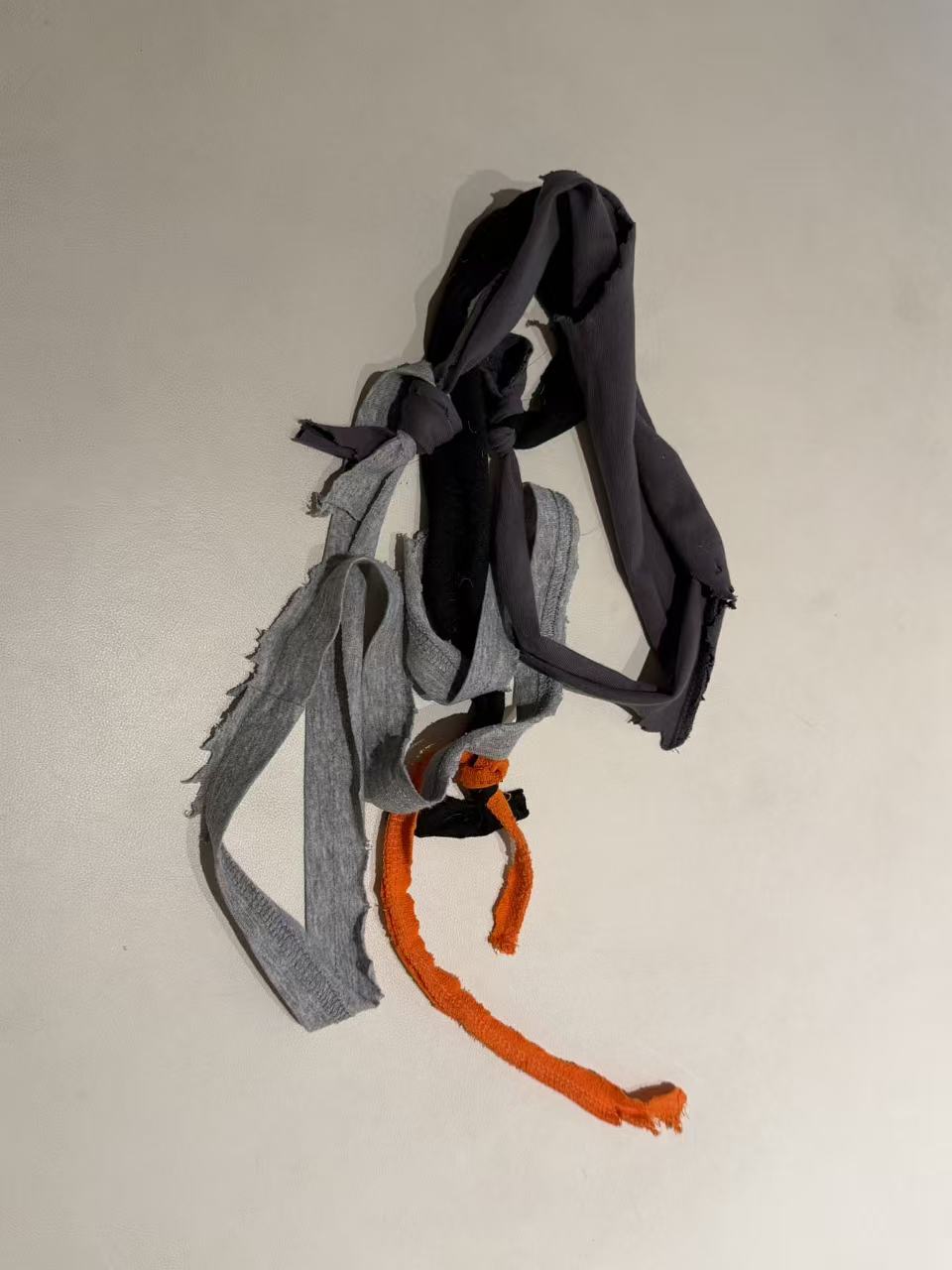 Grey, dark and orange fabric strips connected with knots.